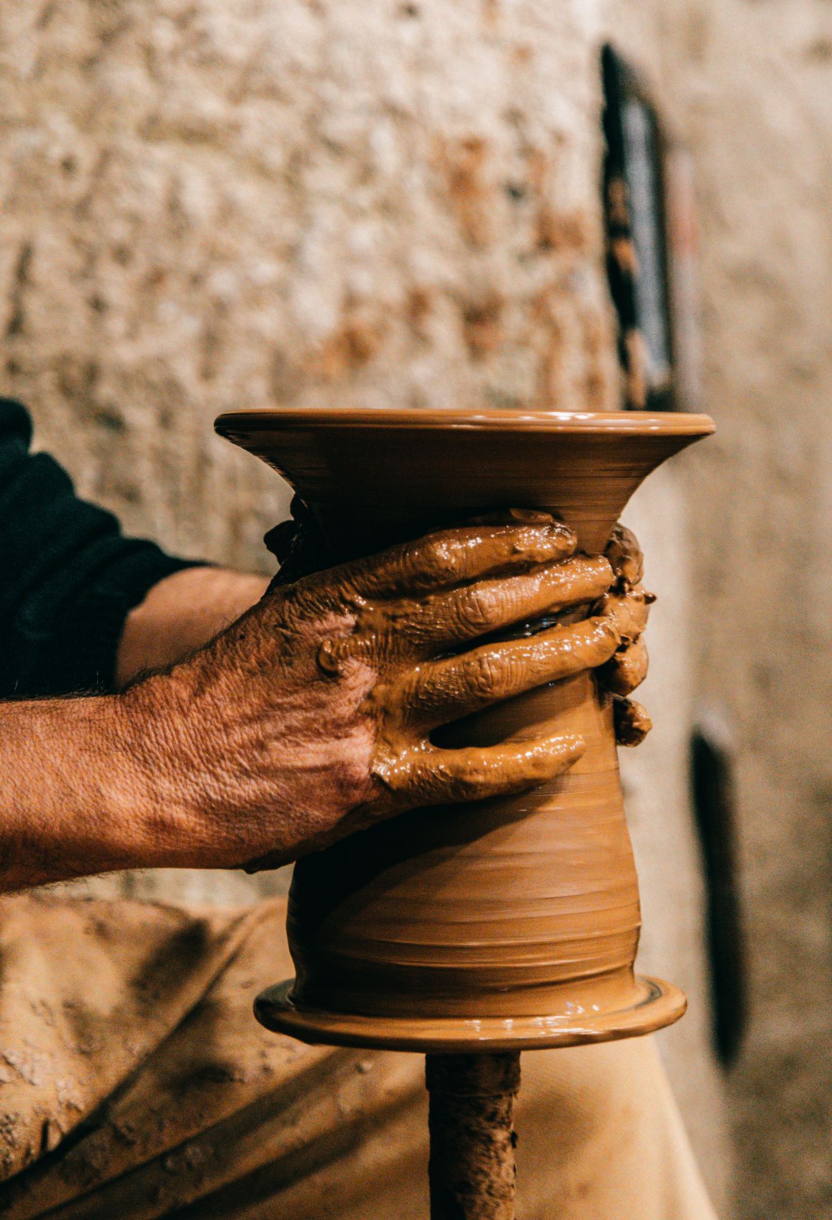 An artisan shapes a clay vessel by hand on a pottery wheel.