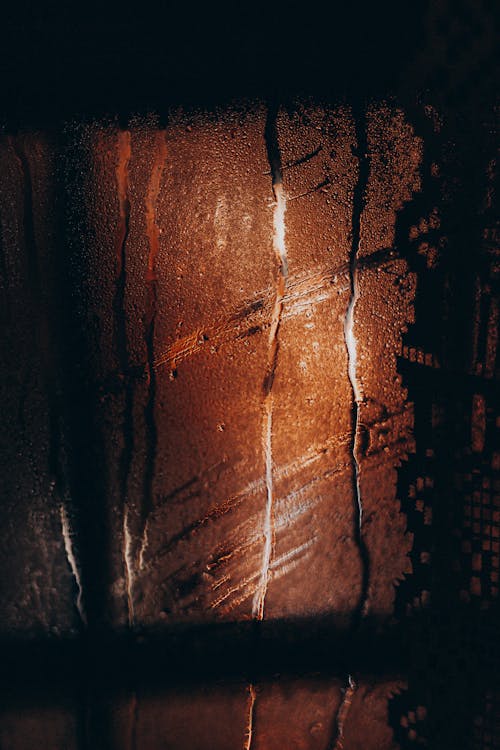 Water drops flowing on misted glass window during rain in cold dark evening