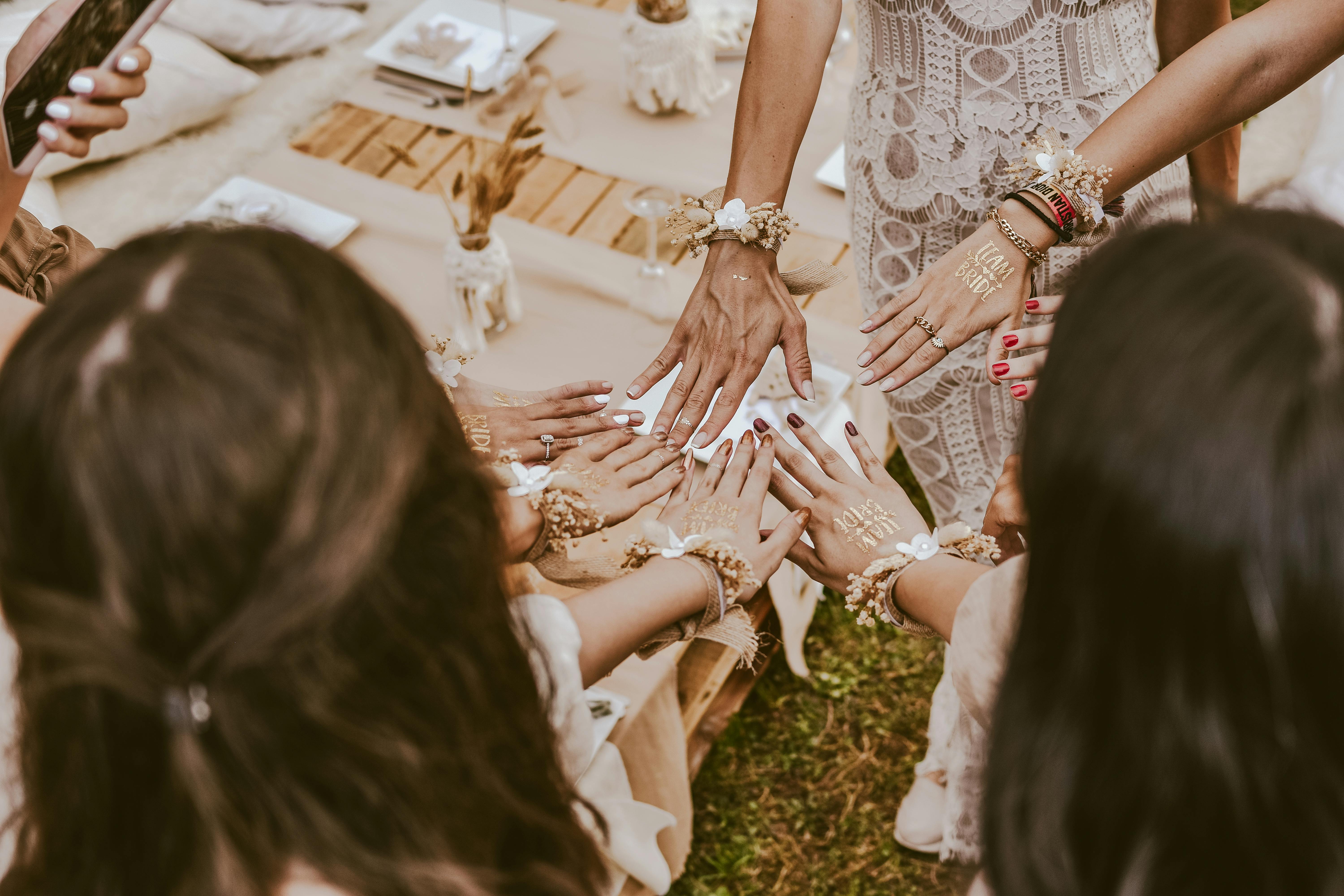 A group of bridesmaids at a bachelorette party showing hands with decorative henna and accessories, creating a joyful moment.
