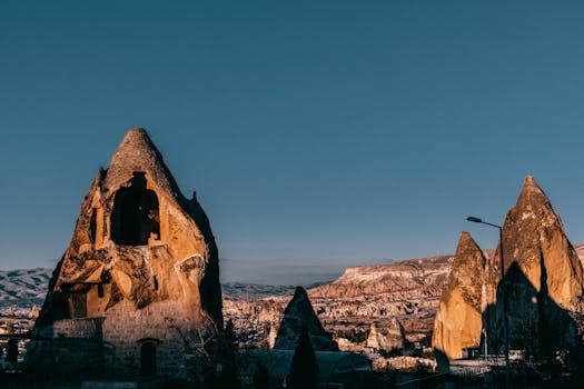 Famous rocky formations with holes and rough surface located in ancient Cappadocia town near hilly terrain against blue sky in Turkey