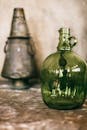 Bottle with green transparent glass placed on concrete surface with metallic incense burner near wall on blurred background in old city