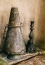 Cone shaped oriental iron incense burner with curving placed near blurred authentic black candlestick near stone wall on rough surface