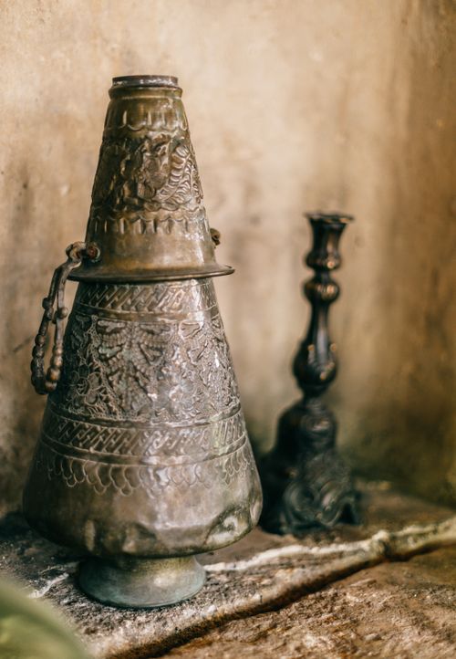 Free Cone shaped oriental iron incense burner with curving placed near blurred authentic black candlestick near stone wall on rough surface Stock Photo