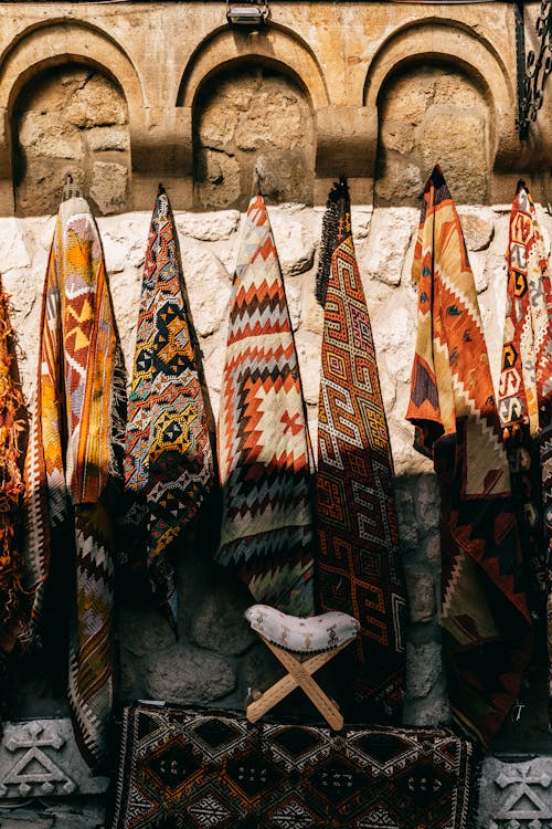 Free Various colorful traditional carpets with ornamental elements hanging on shabby stone wall on bazaar of ancient town on sunny street Stock Photo