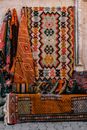 Colorful oriental rugs hanging on wall near sofa with bright cushions with patterns on exhibit in street of old town