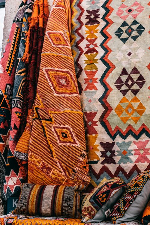 Free Bright rugs with ornamental elements hanging on wall near sofa with colorful cushions on market in old town on street Stock Photo