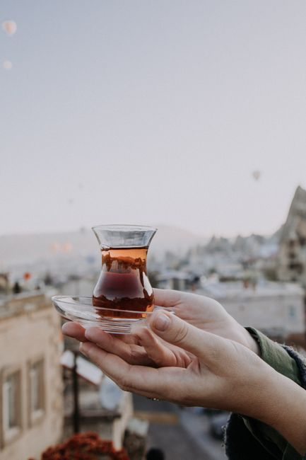 Unrecognizable person with plate and glass filled with hot tea against blurred background of old town with buildings and cloudless sky