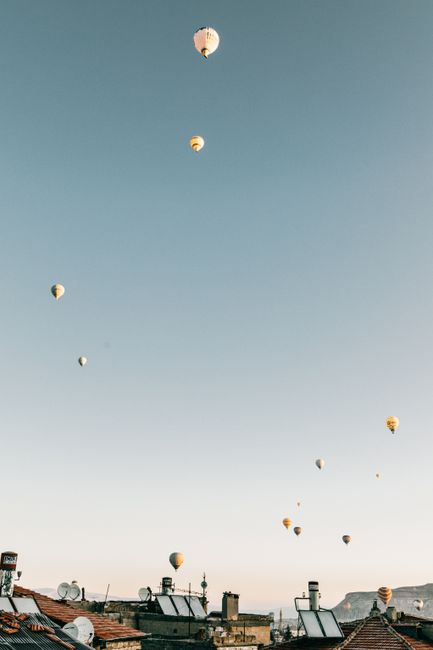 From below of colorful hot air balloons flying high in cloudless blue sky in over city in daylight