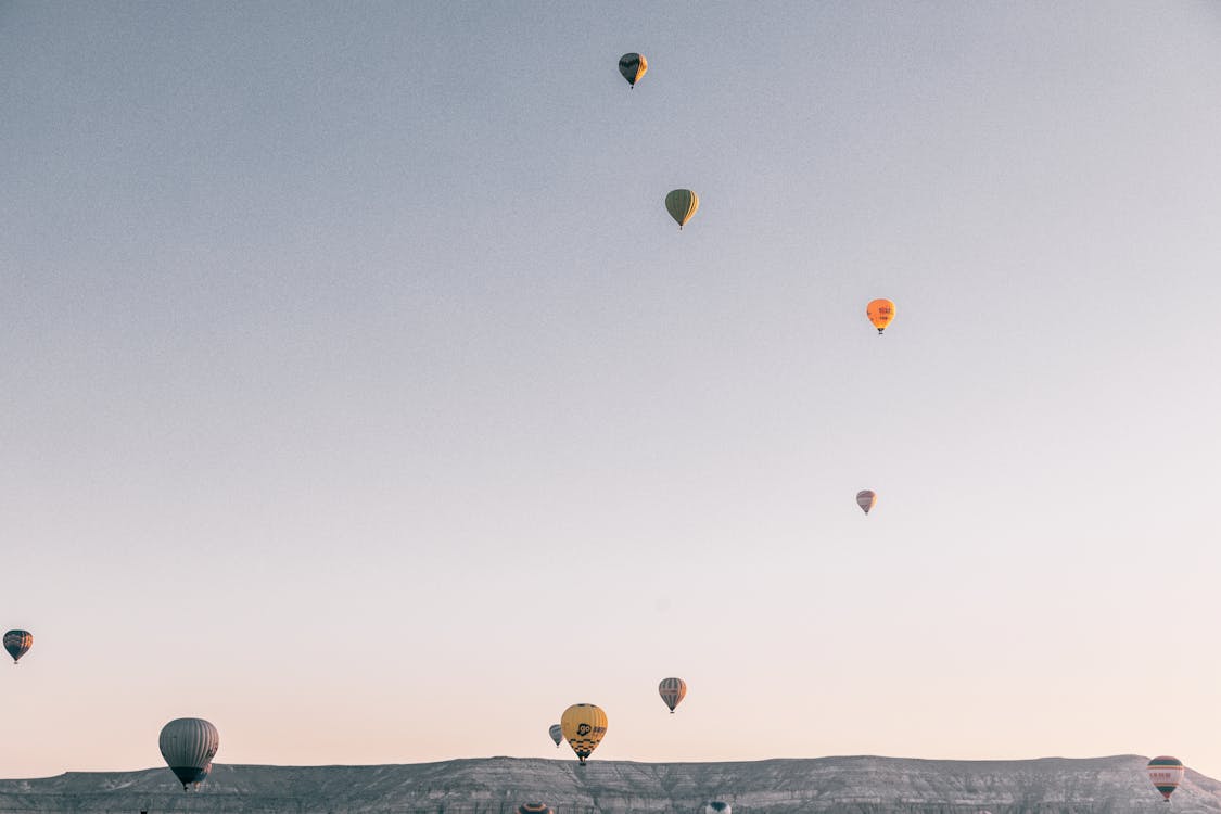 Low angel of various colorful air balloons flying in cloudless sunset sky over rocky mountains