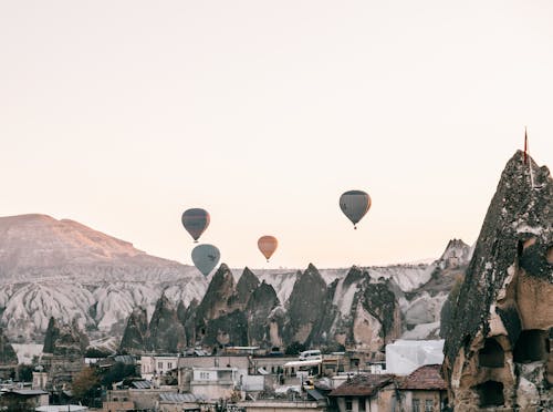 Air balloons flying over town located amidst rocky formations at sundown