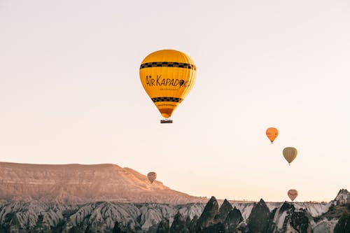 Free From below of colorful air balloons flying over rocky formations in Goreme National Park located in mountainous valley against cloudless sundown sky Stock Photo