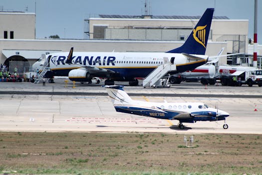 Civil utility and narrow body aircraft parked on runway tracks near modern airport building against cloudless blue sky