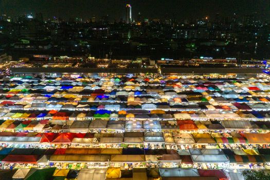 Vibrant aerial view of a bustling night market in Thailand with colorful tents and city skyline.