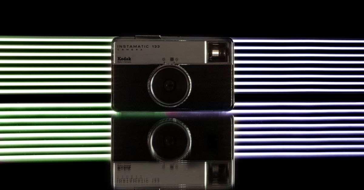 Stylish composition of old fashioned film photo camera on black table against dark background with glowing white lines