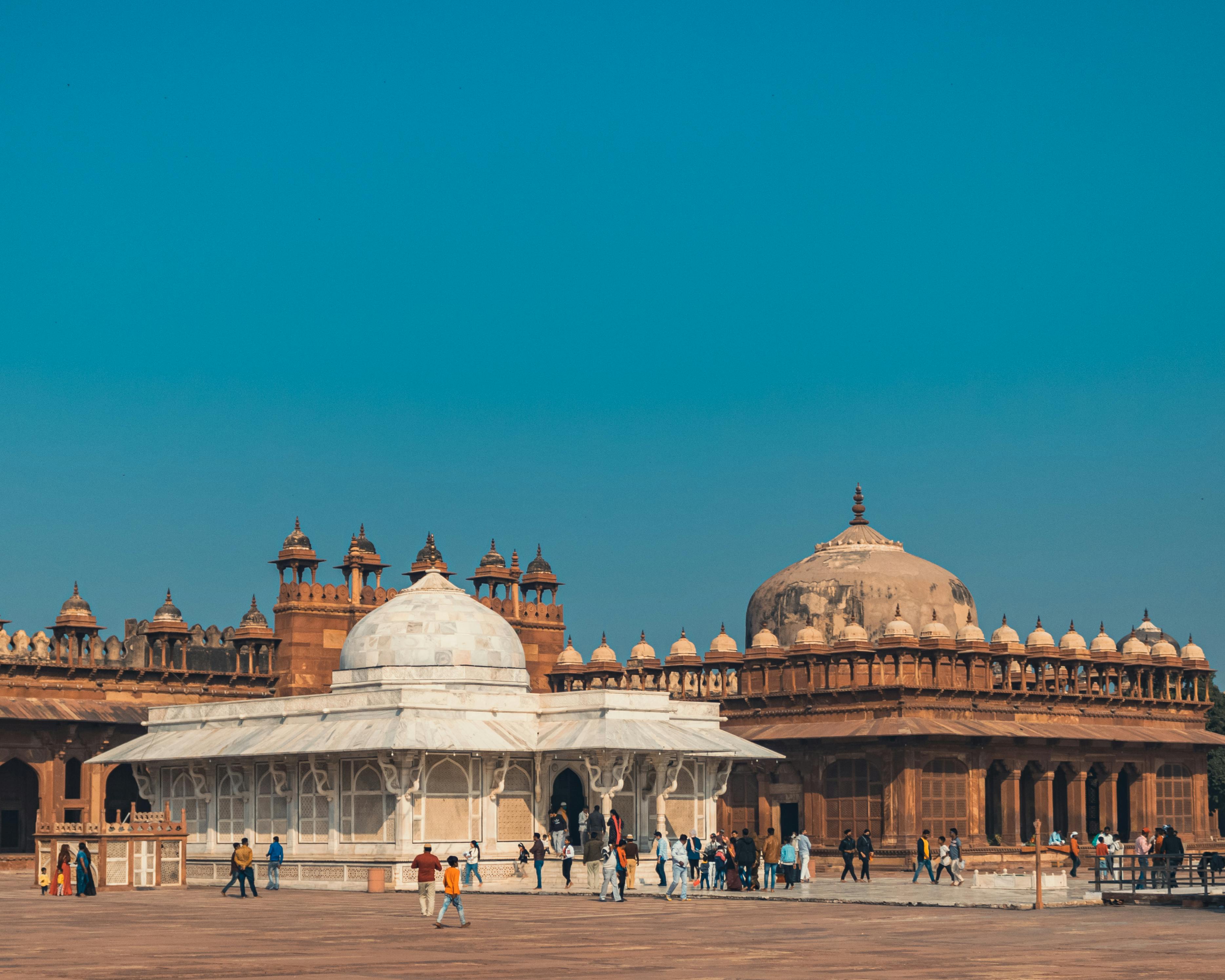 Tourists explore the historic architecture of Fatehpur Sikri under a clear blue sky.