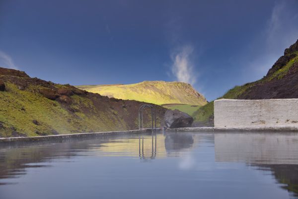 Steaming geothermal bathing pool below green hills — photo by Koen Swiers on Pexels
