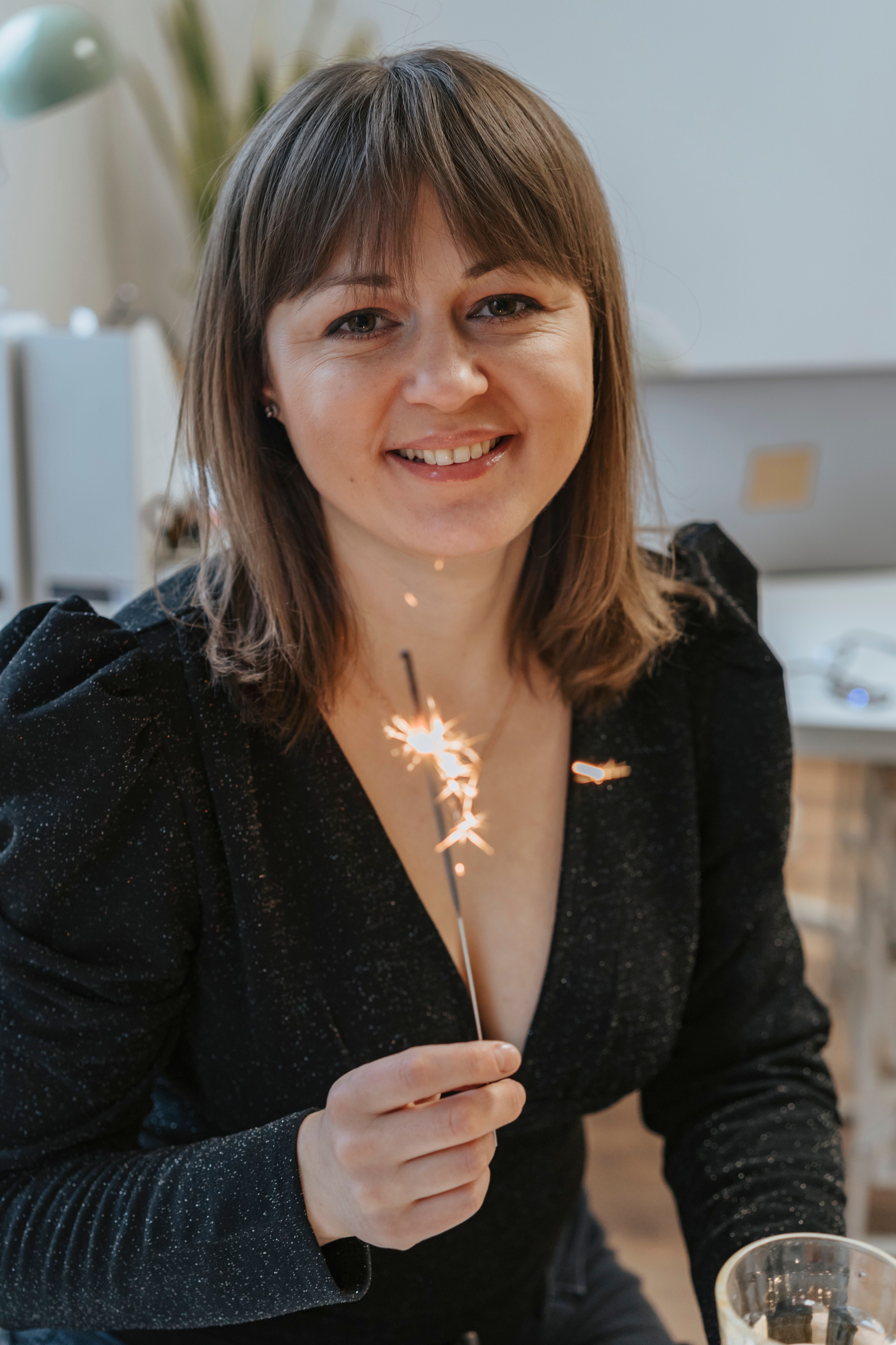 Caucasian woman smiling while holding a sparkler indoors, creating a festive atmosphere.
