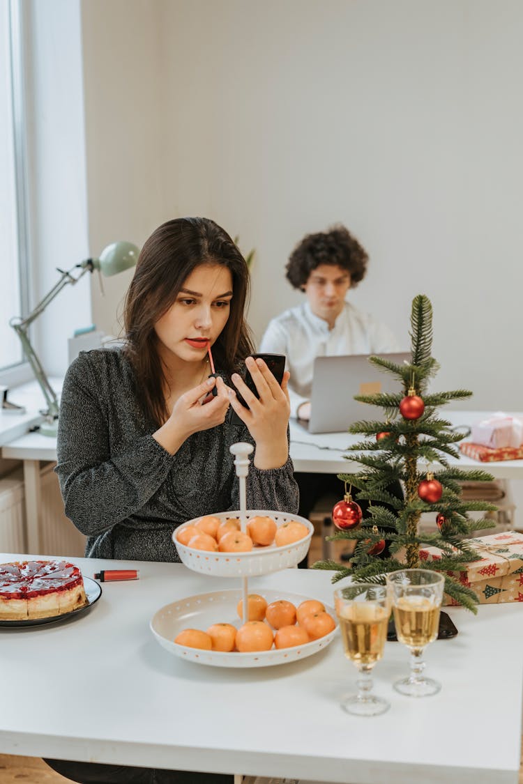 Photo Of A Woman Applying Lip Tint On Her Lips Near A Christmas Tree