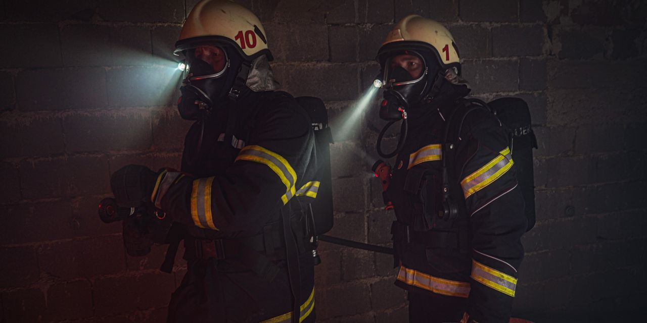 Firefighters in full gear working in dark conditions with flashlights.