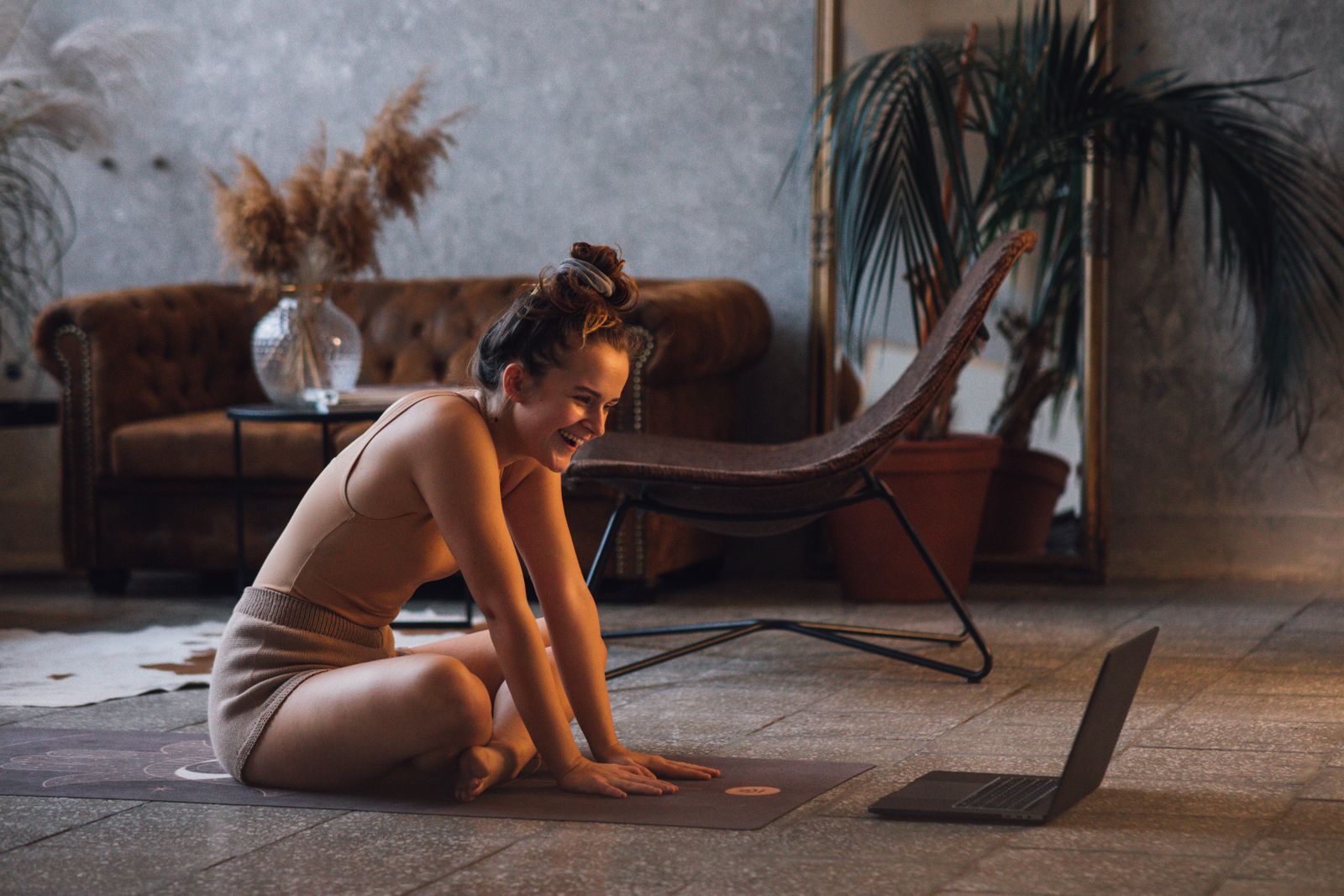 Smiling woman on a yoga mat using a laptop for a live online yoga class in her living room