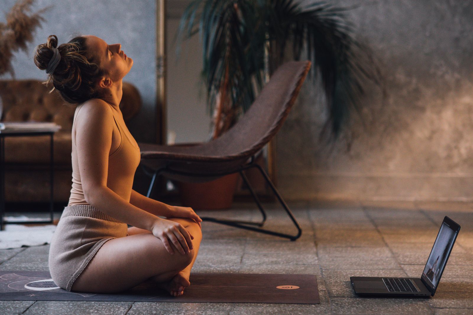 Woman on a yoga mat at home following an instructor-led session on her laptop