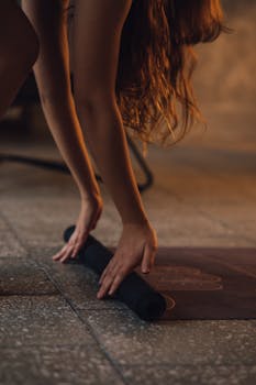 Close-up of woman rolling a yoga mat, dimly lit indoor setting. Relaxing and calm atmosphere.