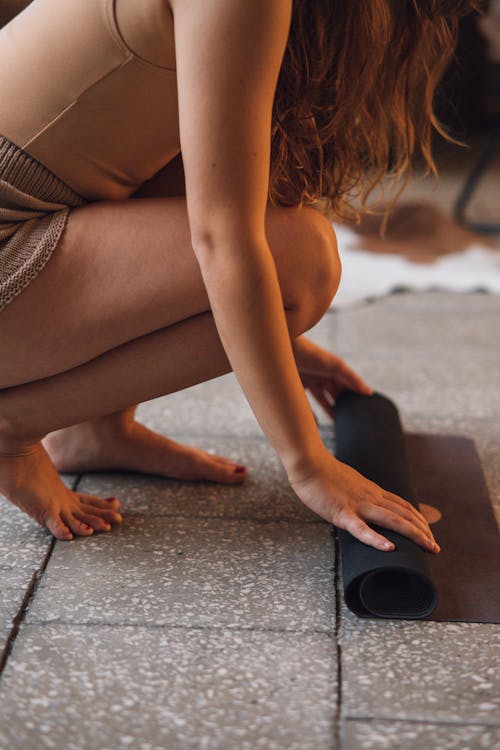 Photo of a Woman Crouching while Rolling a Black Yoga Mat