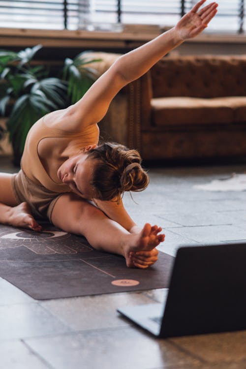 Woman in a Beige Top Stretching Near a Laptop