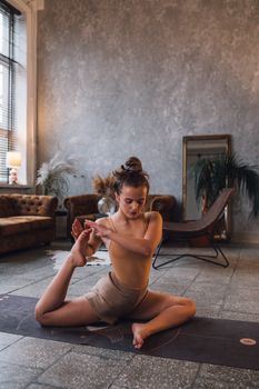 Young woman practicing yoga indoors, performing a stretching exercise on a yoga mat.