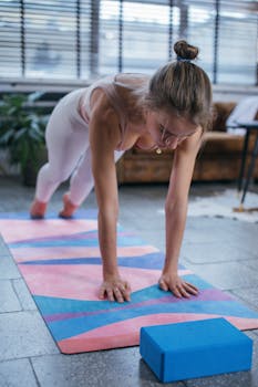 A woman performing yoga indoors, focused on a yoga mat with a block, showcasing healthy living.