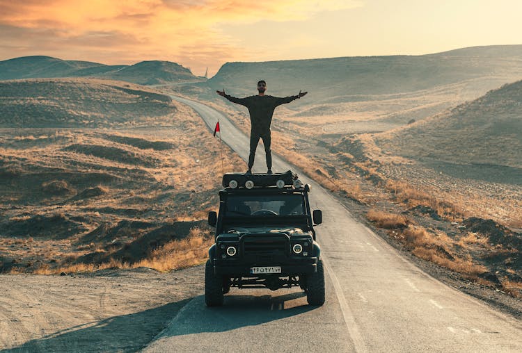 Male Standing On Car Roof In Majestic Mountains