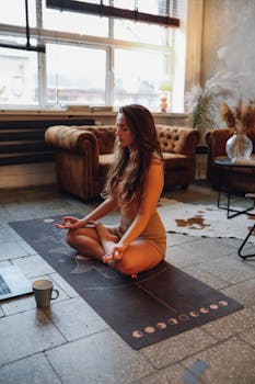 A woman practices meditation in a cozy indoor setting, seated on a yoga mat.