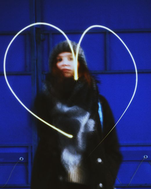 Blurred portrait of a woman with light painting creating a heart shape, set against a blue backdrop.