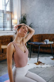 A woman in a beige tank top practices yoga at home, embodying calmness and relaxation.