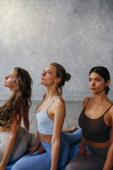 Three women in athletic wear engaged in a yoga session indoors, focusing on wellness and mindfulness.