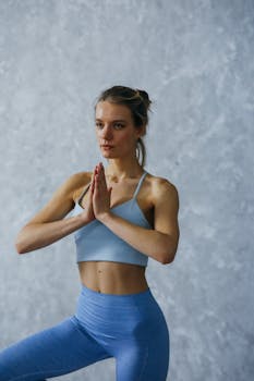 A woman in activewear performing a yoga pose indoors with a serene expression.