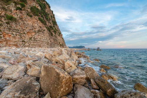 Free Cliff surrounded with heavy rough stones washed by ocean Stock Photo