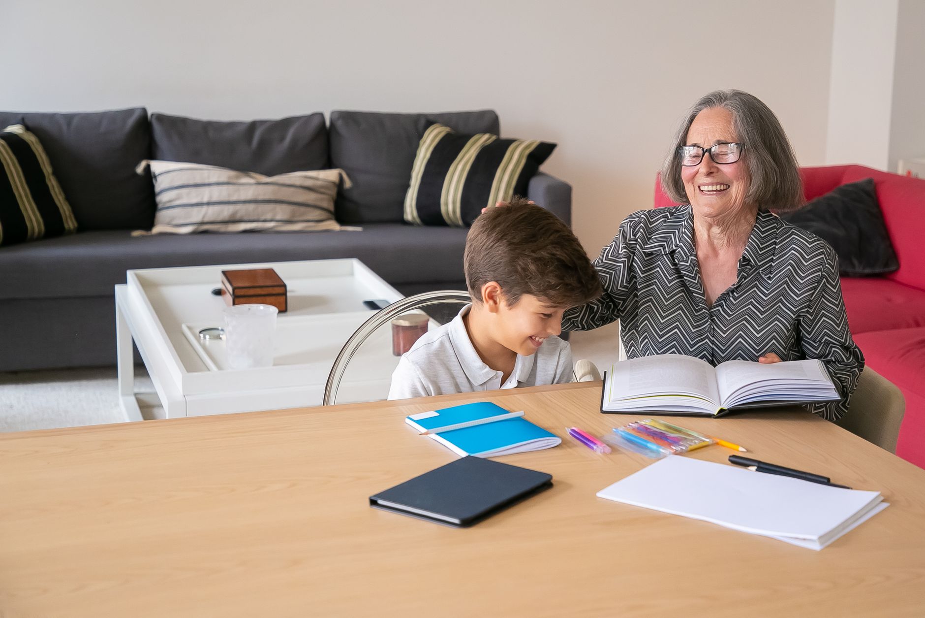Happy grandmother assisting her grandson with homework indoors, creating a joyful learning atmosphere.