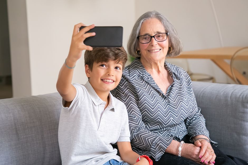 Happy grandmother and grandson enjoying a selfie moment on the couch indoors