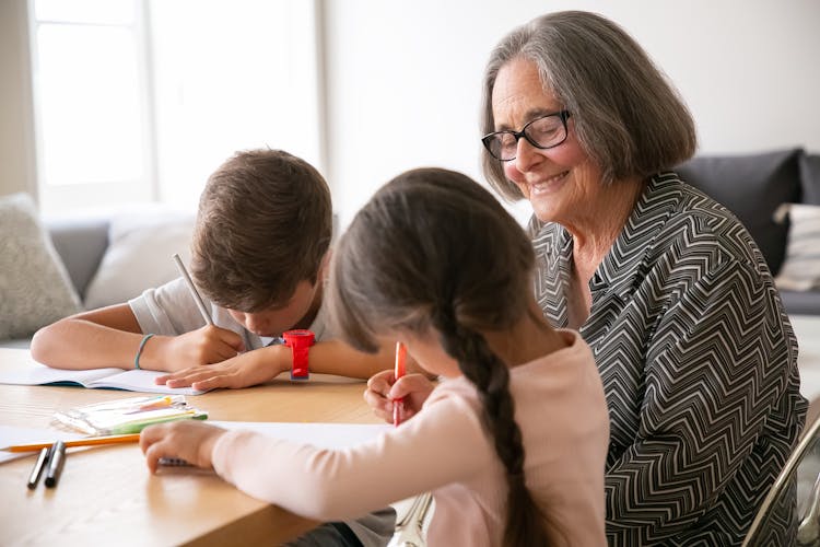 Elderly Woman And Kids Drawing At A Table 