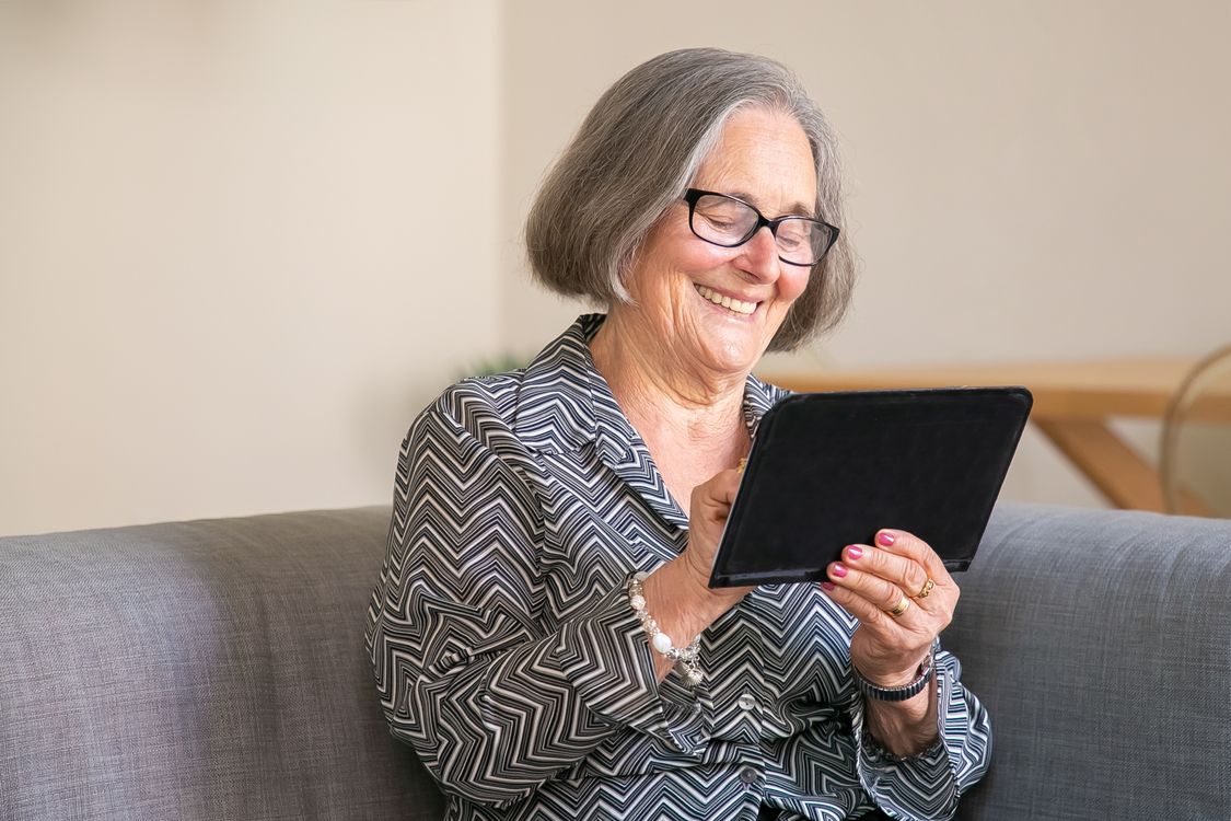 An older woman smiling at her tablet, looking relaxed and confident