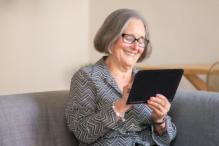 An Elderly Woman Holding A Tablet Smiling