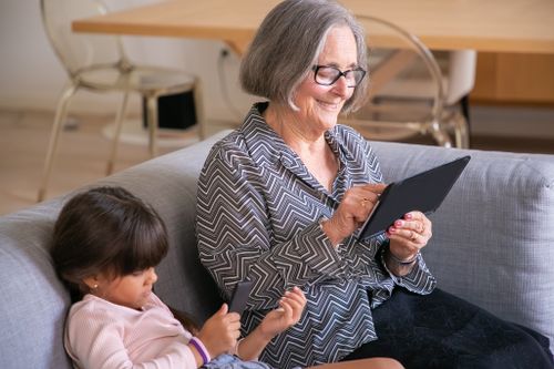 Free A senior woman and a young girl on a sofa interacting with a tablet indoors. Stock Photo