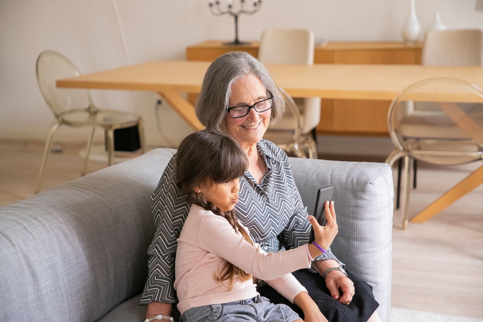 A grandmother and her granddaughter smiling together on a couch