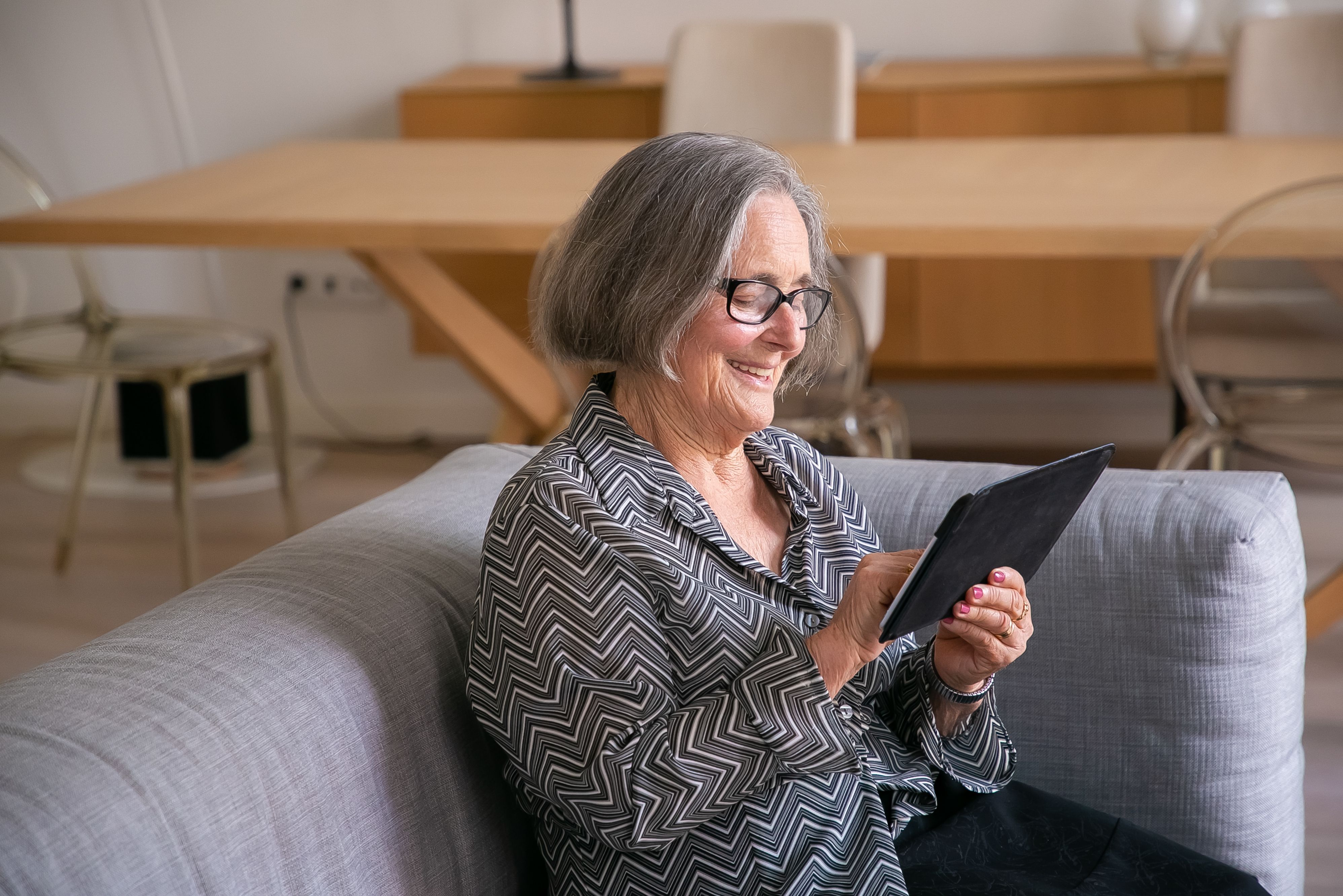An older woman smiling while using a large-screen tablet in her living room