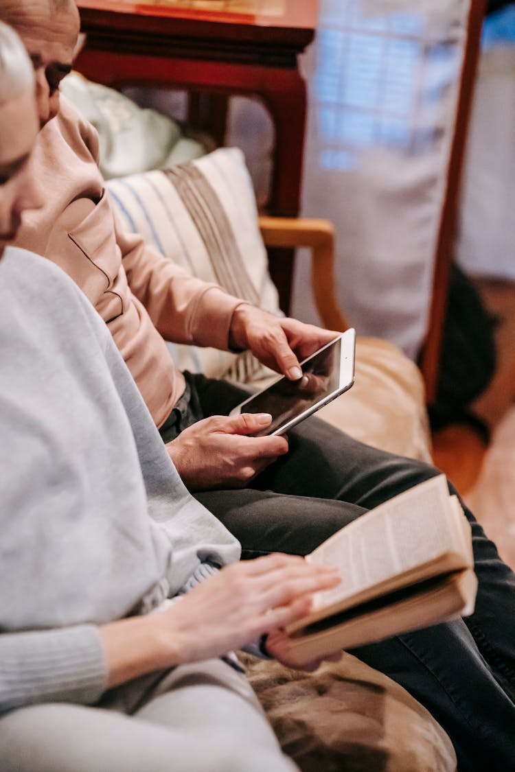 Anonymous Spouses Resting On Sofa With Book And Tablet During Weekend