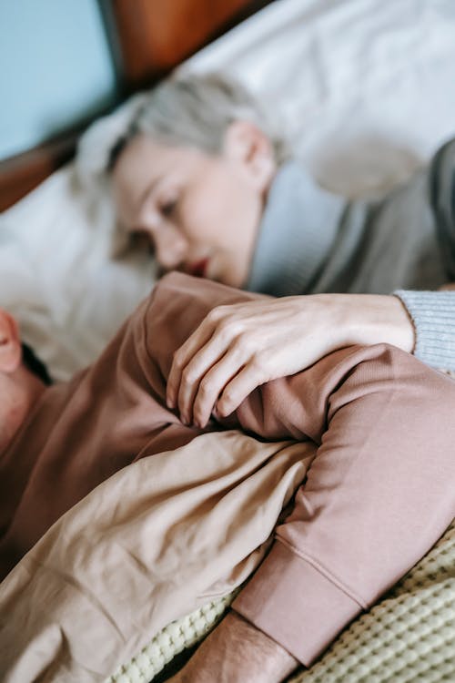 Free High angle of female with short dyed hair in warm clothes lying on comfortable bed while sleeping with unrecognizable husband at home Stock Photo
