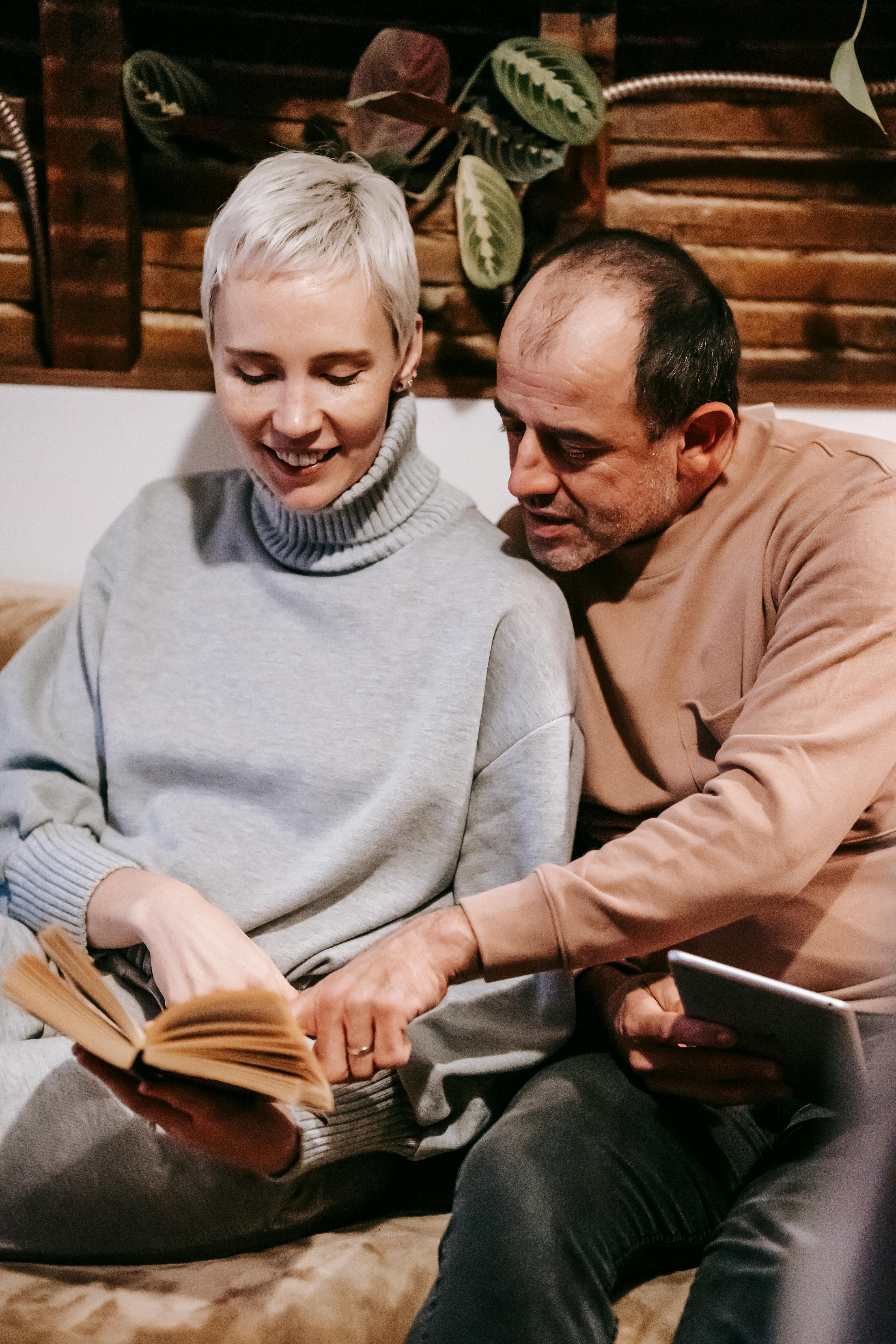 positive adult diverse couple reading novel on couch