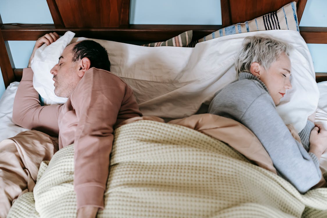 Free From above side view of middle aged diverse spouses in warm clothes sleeping lying back to back in comfortable bed in morning Stock Photo