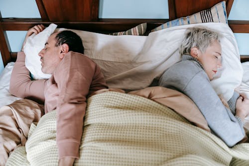 Free From above side view of middle aged diverse spouses in warm clothes sleeping lying back to back in comfortable bed in morning Stock Photo